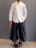White asymmetric long sleeve shirt and black pleated trousers co-ord set on a hanger