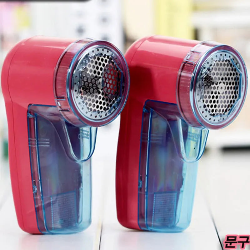 Portable electric clothing lint remover device on a table next to a sweater.