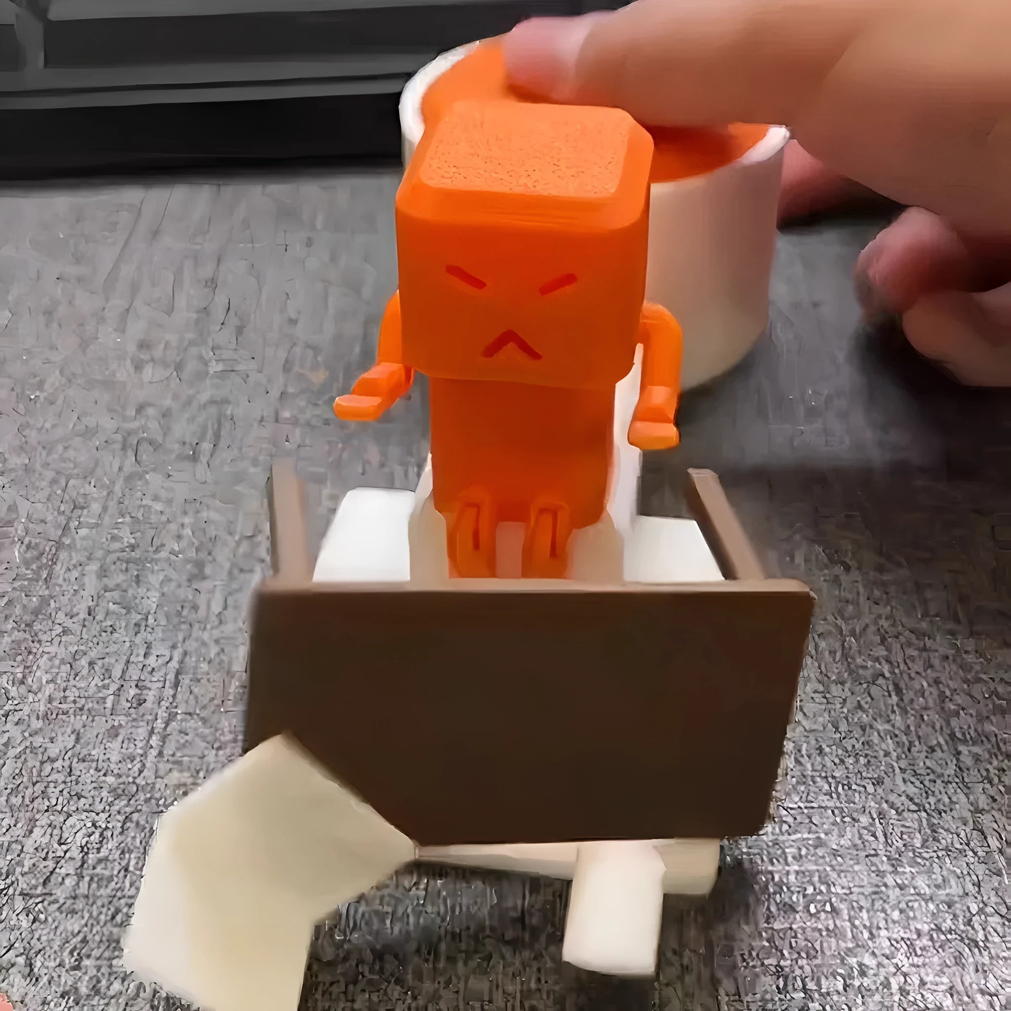Orange plastic decompression toy with a table-turning mechanism on a desk.