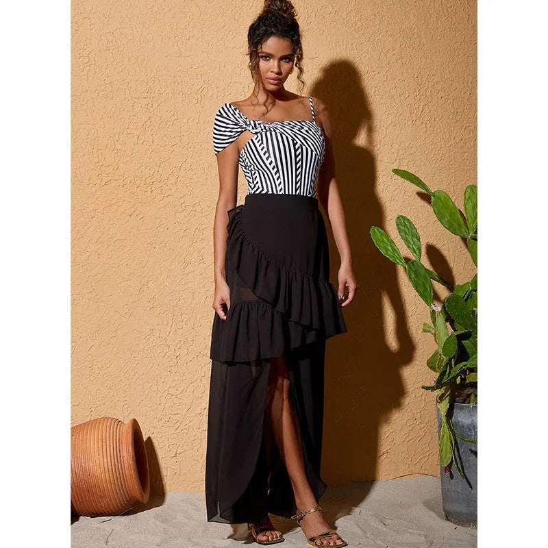 Woman wearing a striped one-piece swimsuit with a black ruffled skirt attached.