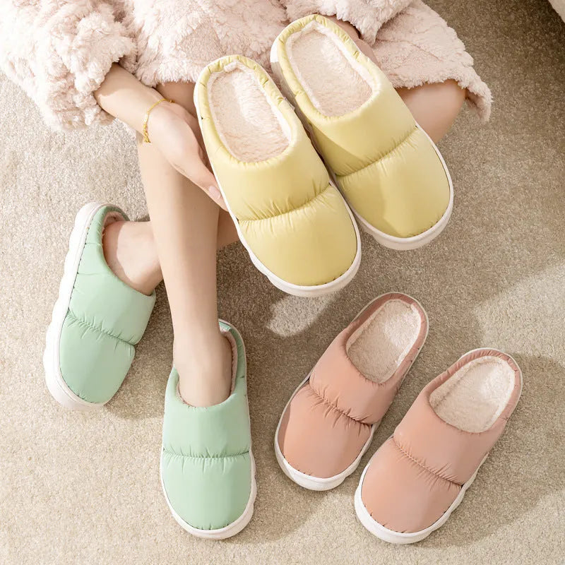 A pair of blue down cotton plush slippers with a thick rubber sole and artificial leather upper, shown on a wooden floor.
