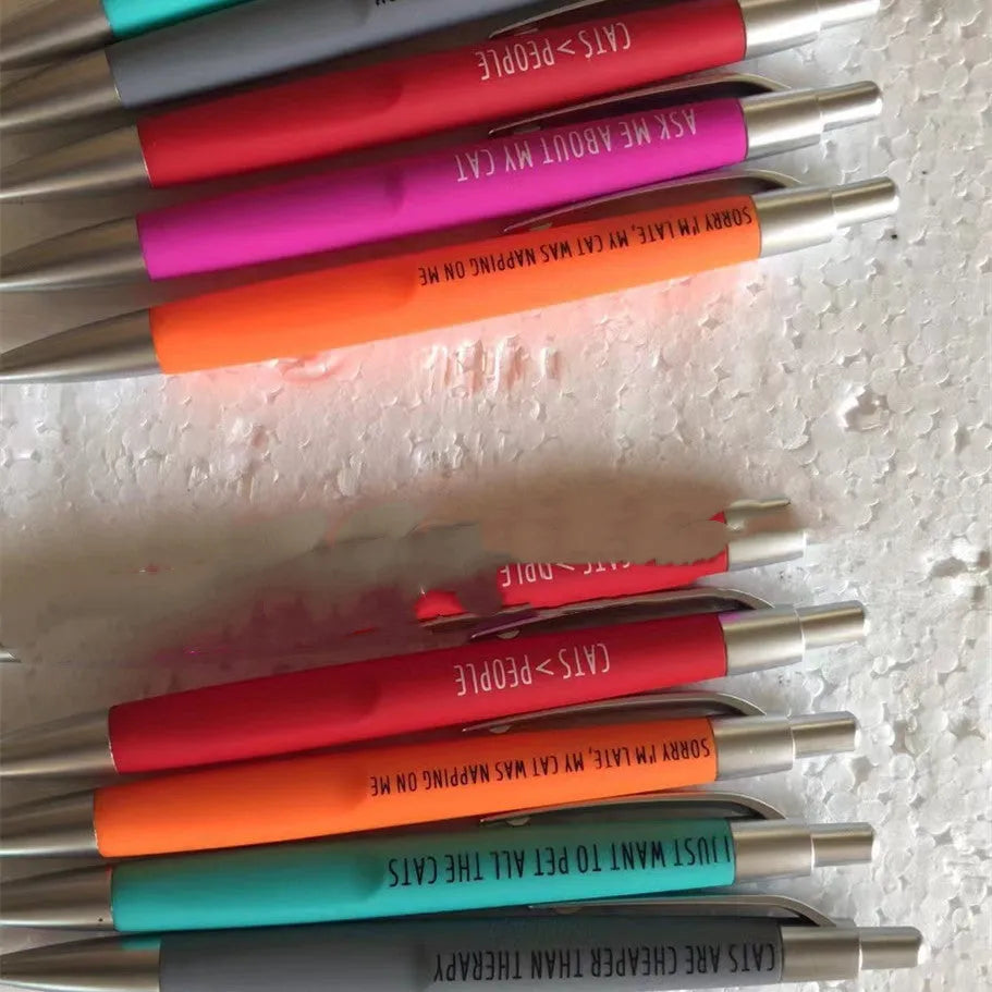 Set of five coloured push action automatic pens in a cat-themed or dog-themed design, next to a beaded storage bag.