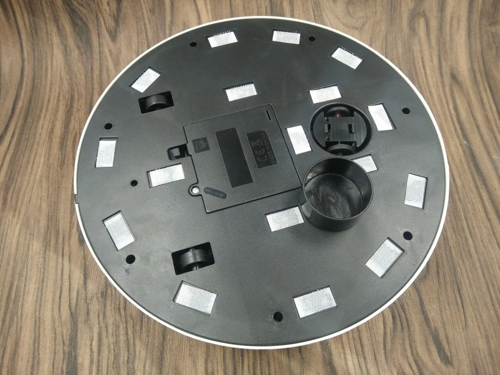 Black or white AC automatic sweeping robot on a hardwood floor next to a dust bin.
