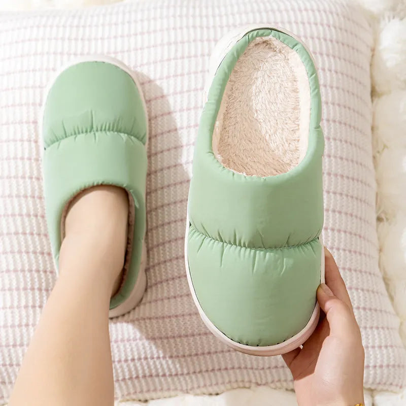 A pair of blue down cotton plush slippers with a thick rubber sole and artificial leather upper, shown on a wooden floor.