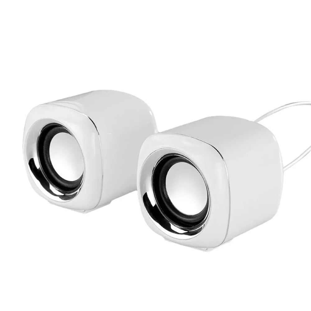 A pair of compact black or white wired desktop computer speakers with a 3.5mm plug, shown next to a laptop.