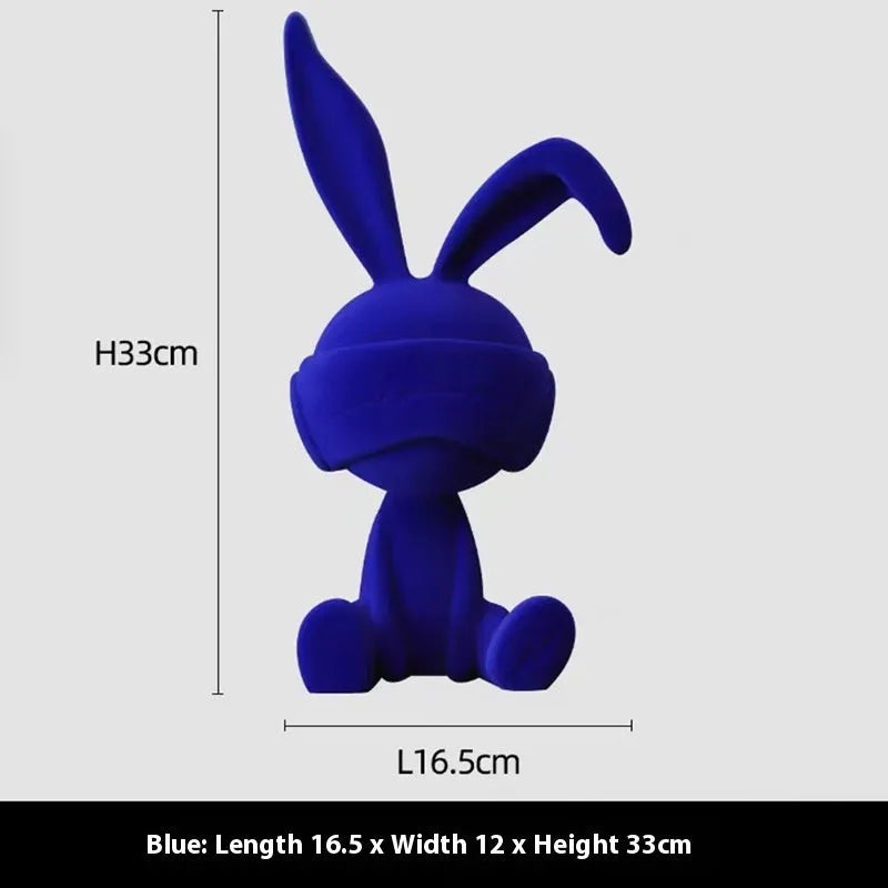 A resin table ornament of a rabbit wearing a suede blindfold, shown in blue, green, and red colour options.
