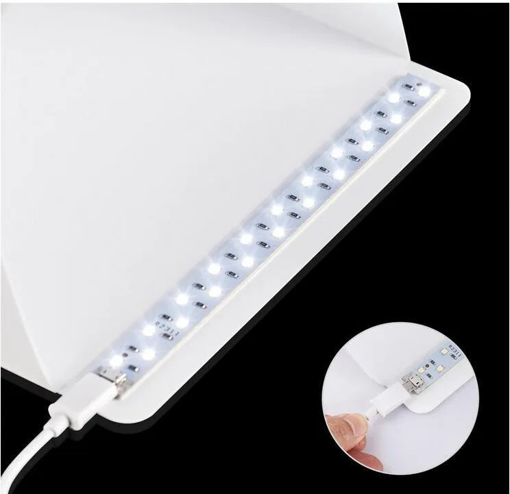 Mini LED folding photo box open with black and white background pads, USB cable, and built-in light for small item photography