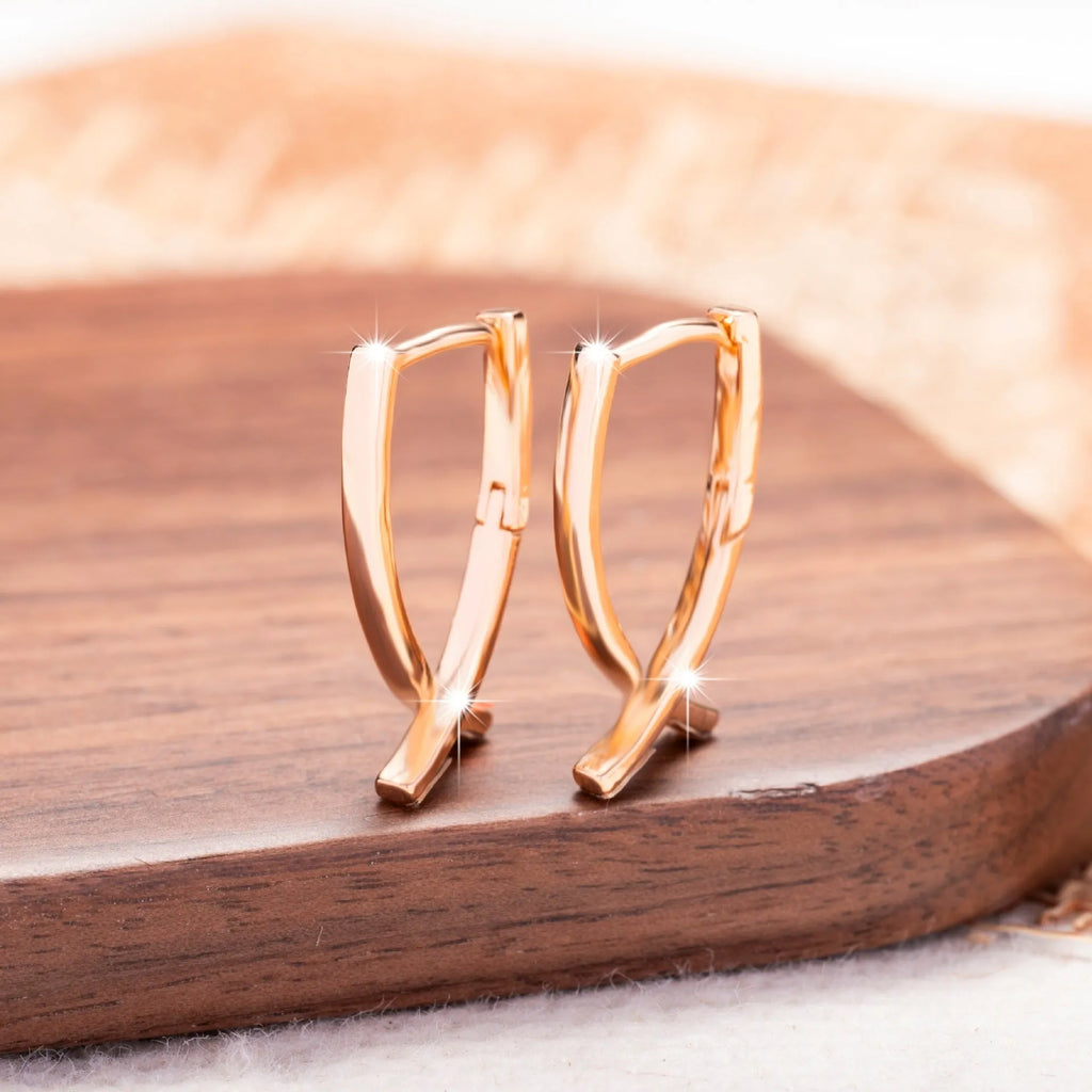 A pair of rose gold coloured cross-shaped stud earrings on a plain background.