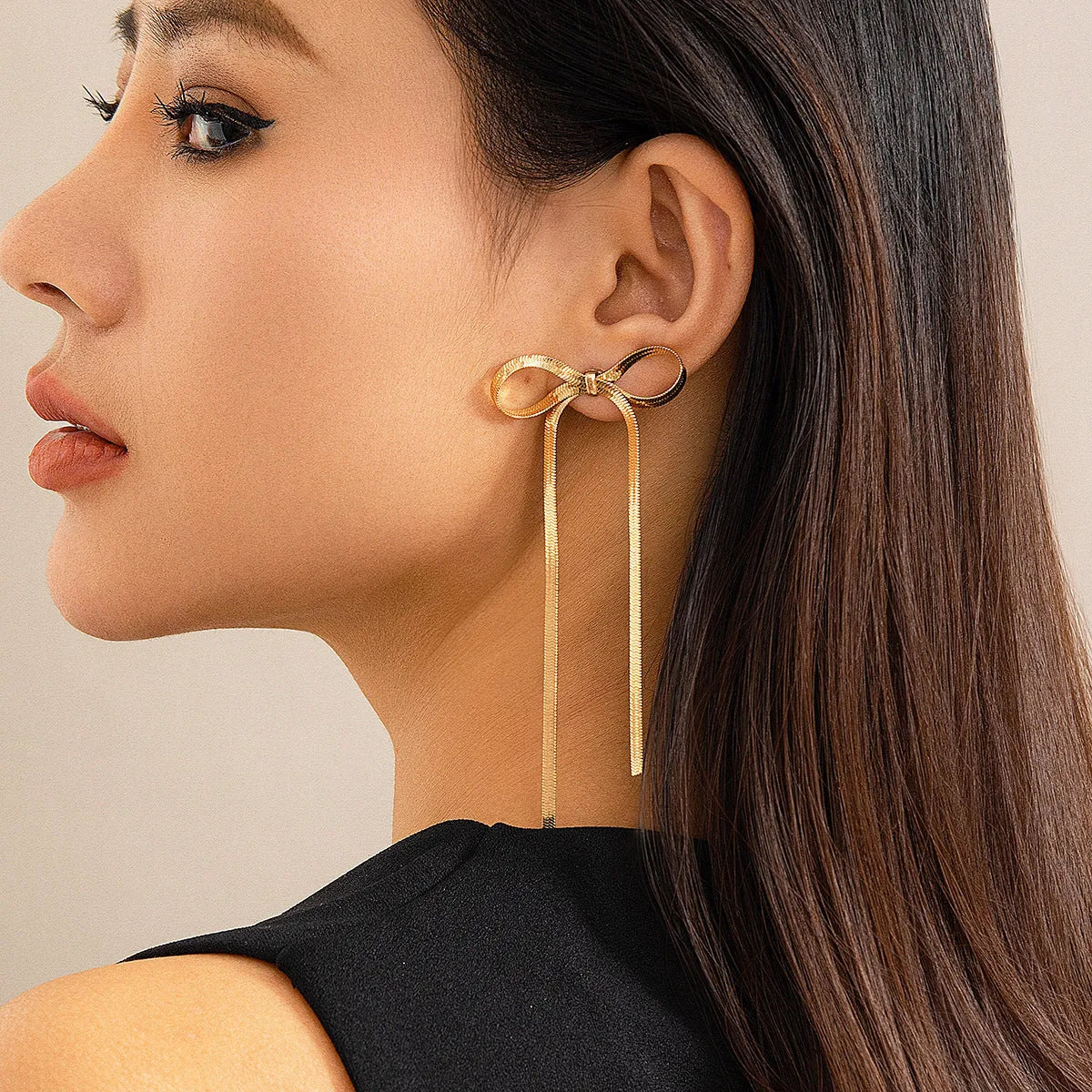 Gold plated bow ribbon dangle earrings with tassel tails on white background
