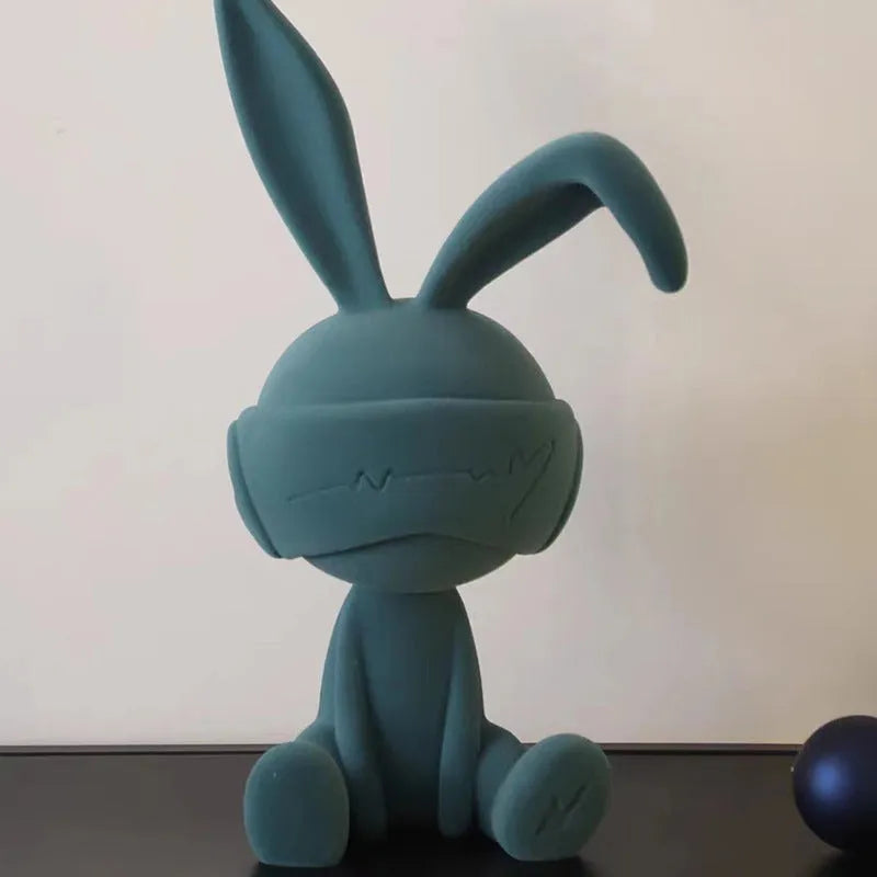 A resin table ornament of a rabbit wearing a suede blindfold, shown in blue, green, and red colour options.
