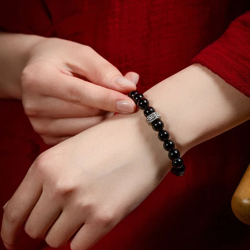Old Pit Obsidian 8mm bead bracelet with zodiac animal charms on a wrist, showing ethnic style and unset inlaid design.