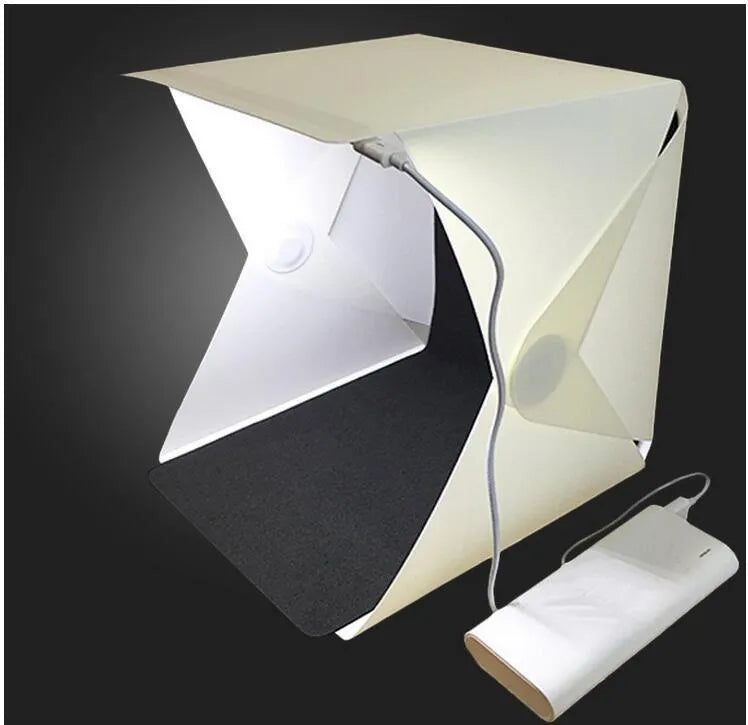 Mini LED folding photo box open with black and white background pads, USB cable, and built-in light for small item photography