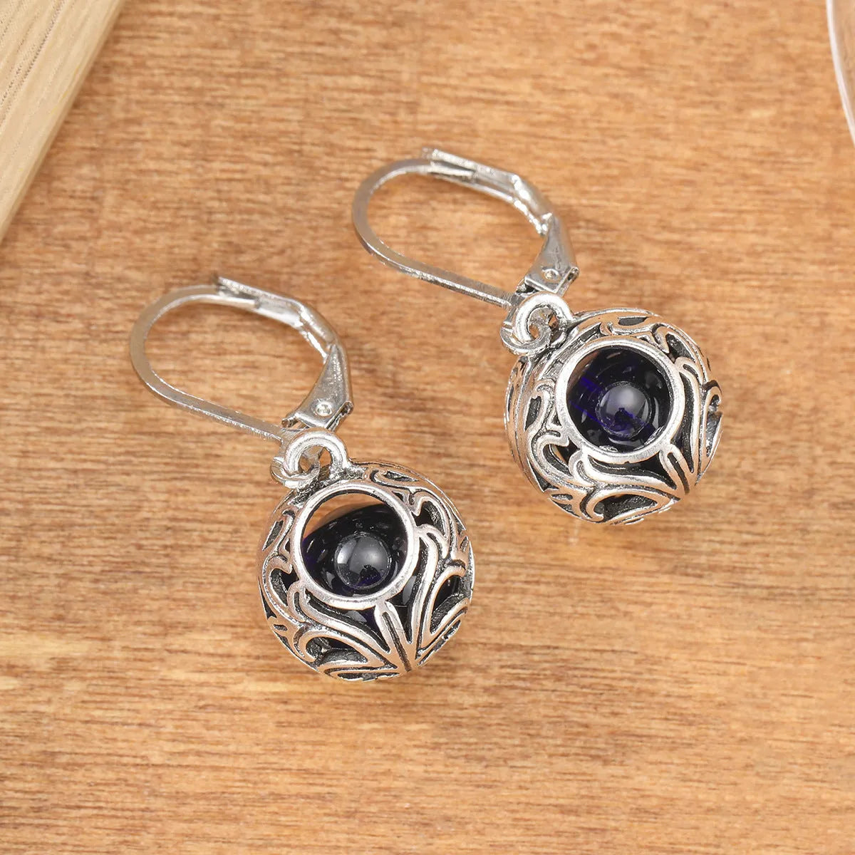 Silver geometric hollow pendant earrings with vintage engraving and a central blue gemstone on a zinc alloy setting.