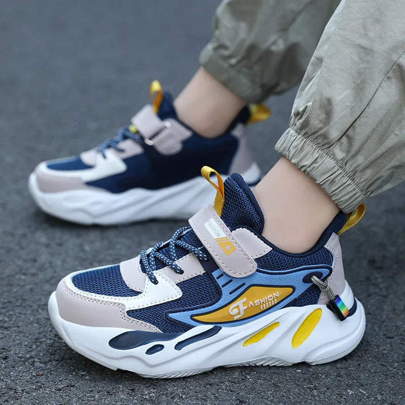 Boys sports running shoes in dark blue with a mesh upper and Velcro strap, shown on a hard ground surface.