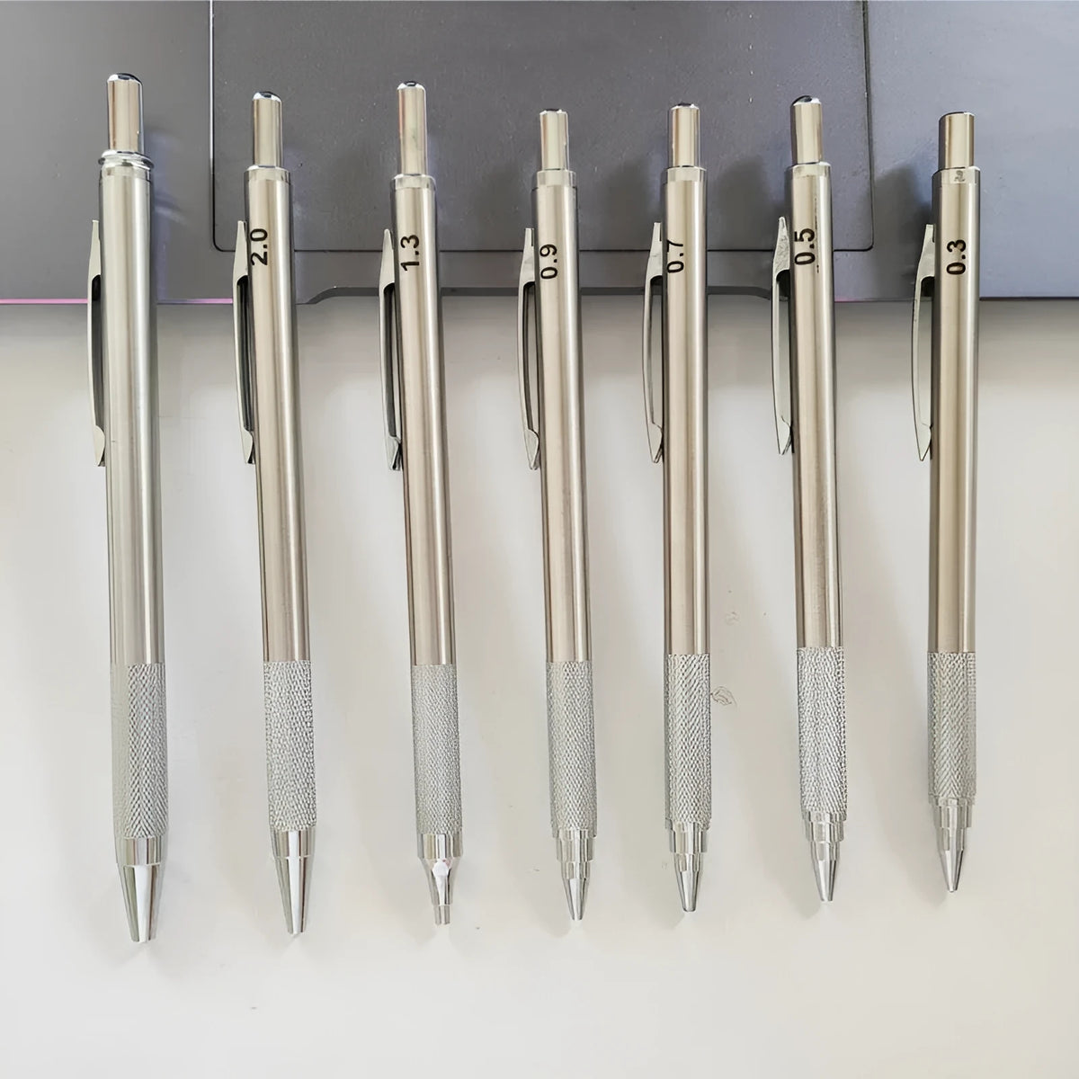 Silver metal automatic mechanical pencil with six compatible lead sizes from 0.5mm to 2.0mm on a notebook.