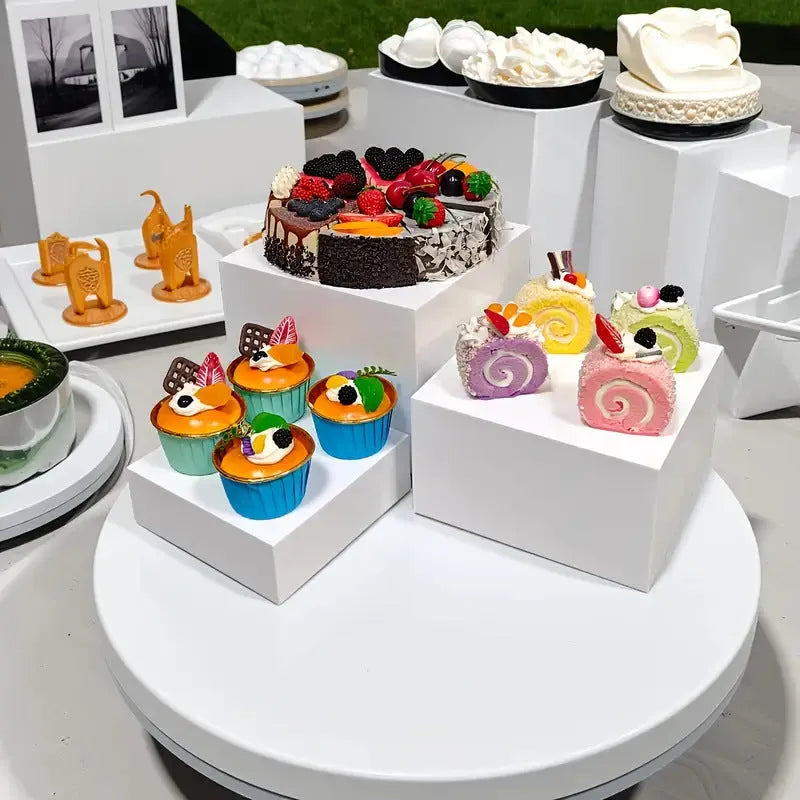 Set of six white plastic cube-shaped dessert display stands arranged on a desktop.