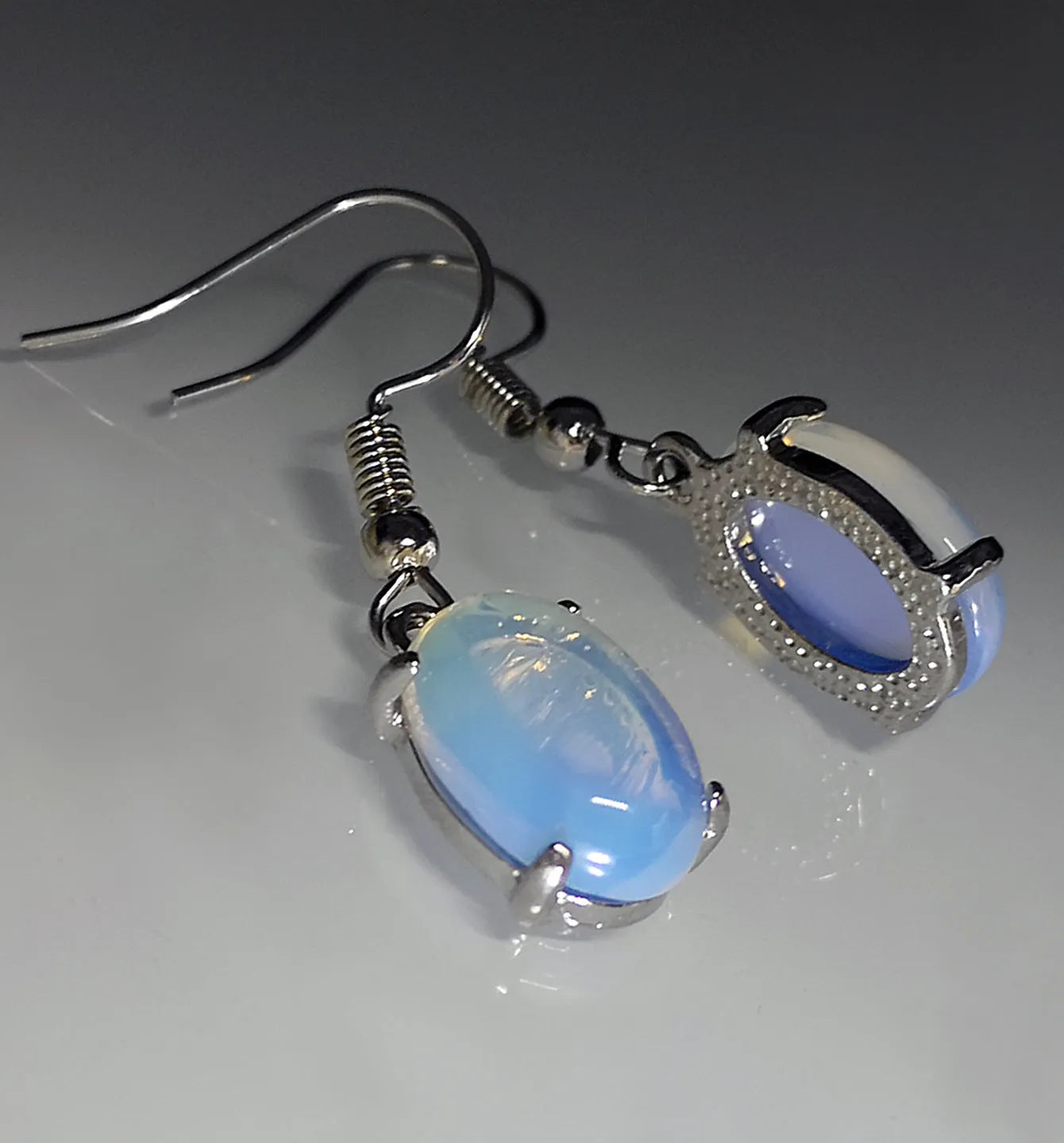 Pair of simple white drop-shaped retro earrings with a moonstone aesthetic on a plain background.