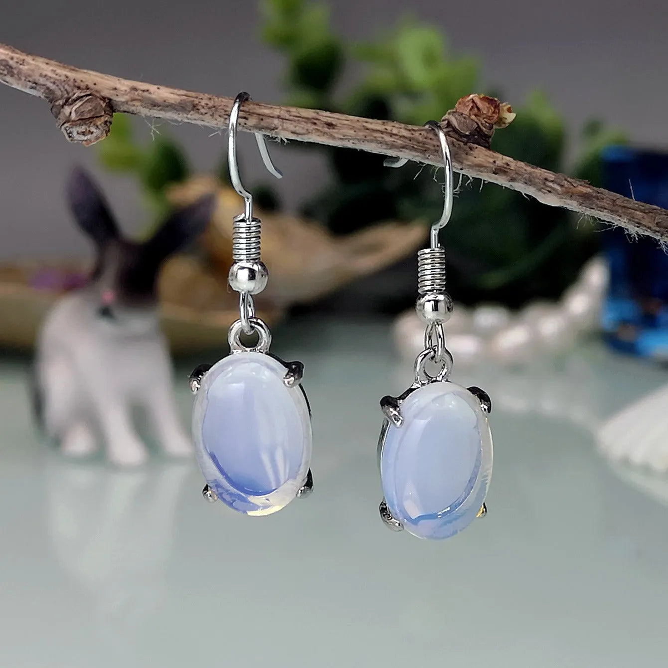 Pair of simple white drop-shaped retro earrings with a moonstone aesthetic on a plain background.