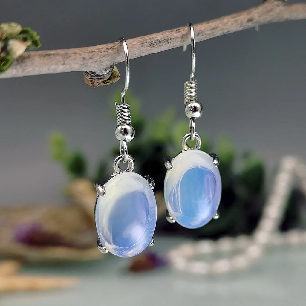 Pair of simple white drop-shaped retro earrings with a moonstone aesthetic on a plain background.