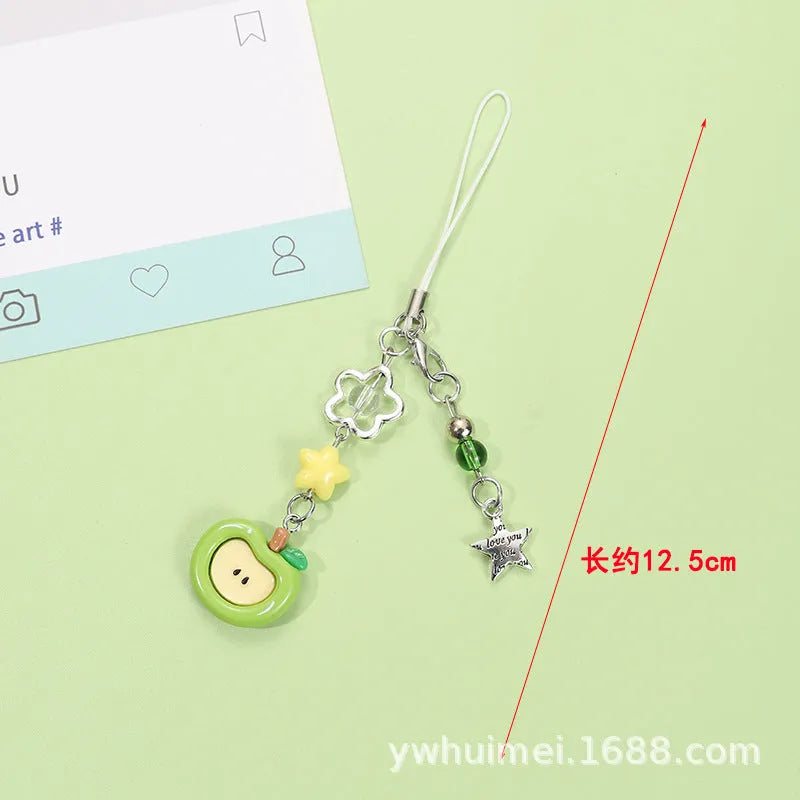 Red apple and strawberry plastic phone charm keychain with white rope on a mobile phone.