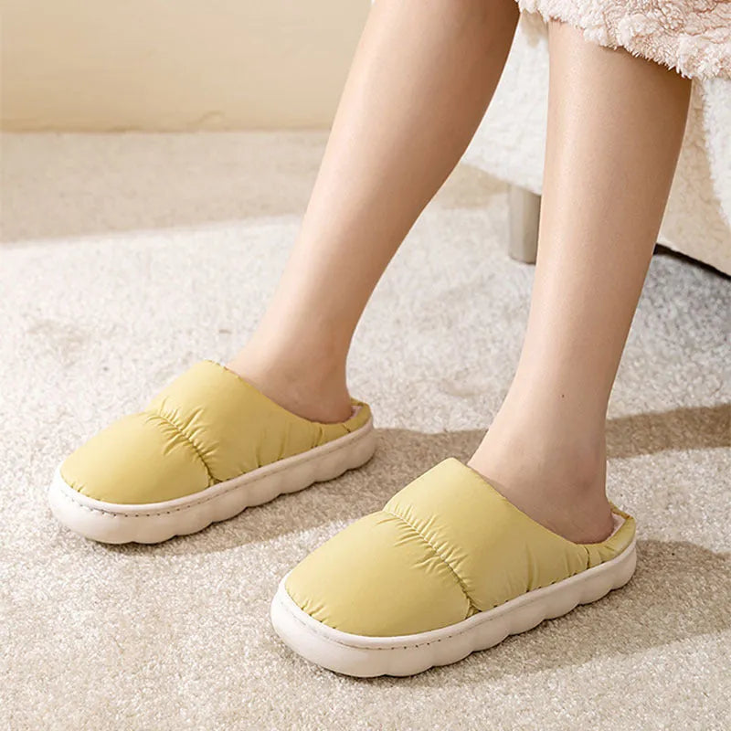 A pair of blue down cotton plush slippers with a thick rubber sole and artificial leather upper, shown on a wooden floor.