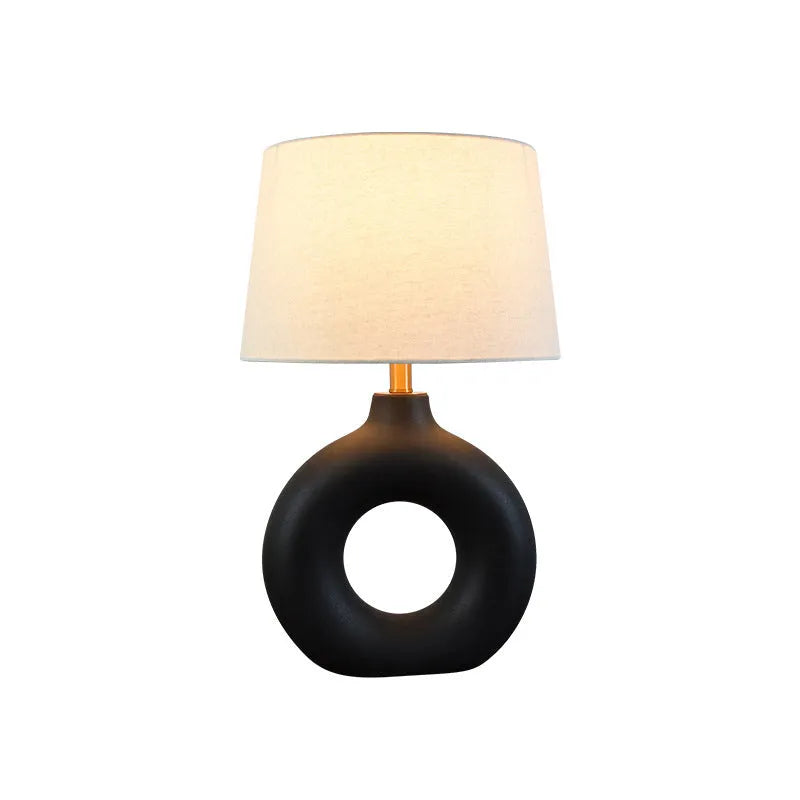 Small white Japanese style pottery pot table lamp with a button switch on a desk.
