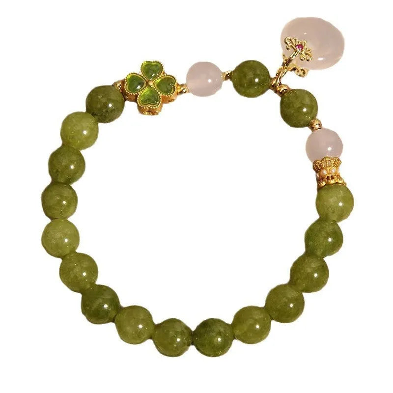 Women's green tourmaline bracelet with a four-leaf clover charm and safety buckle on a wrist.