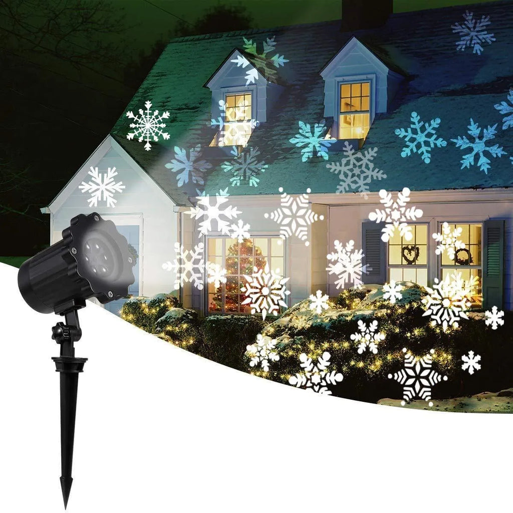 LED Christmas snowflake laser projector with white moving patterns on a dark garden wall at night