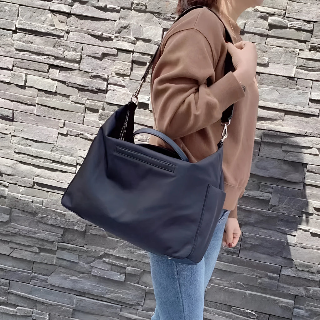 Black nylon waterproof shoulder bag with leather handles showing large open interior.