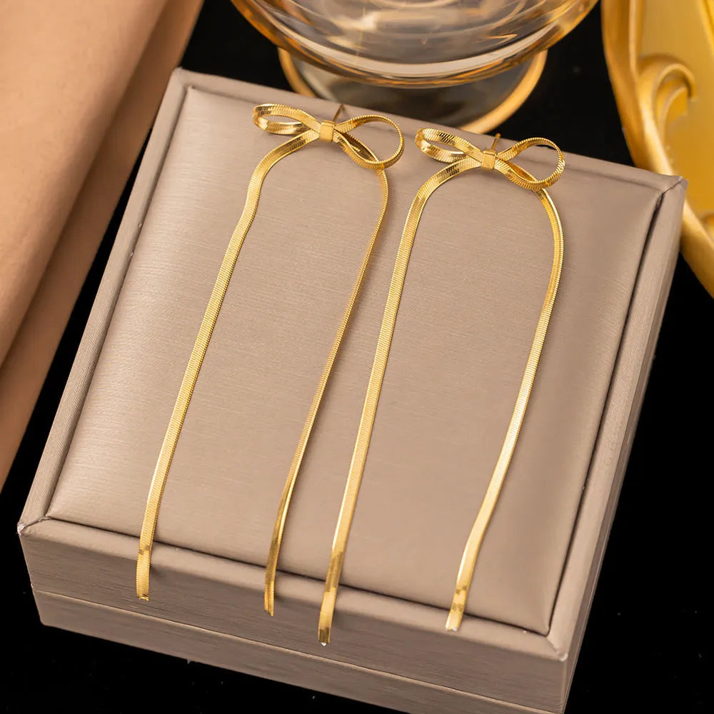 Gold plated bow ribbon dangle earrings with tassel tails on white background
