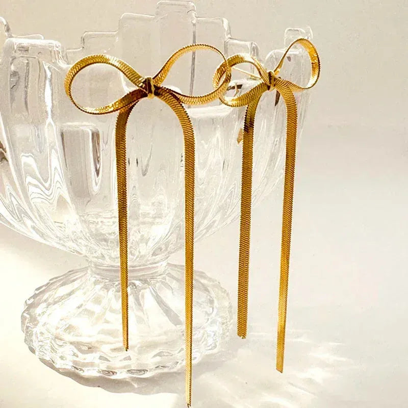 Gold plated bow ribbon dangle earrings with tassel tails on white background