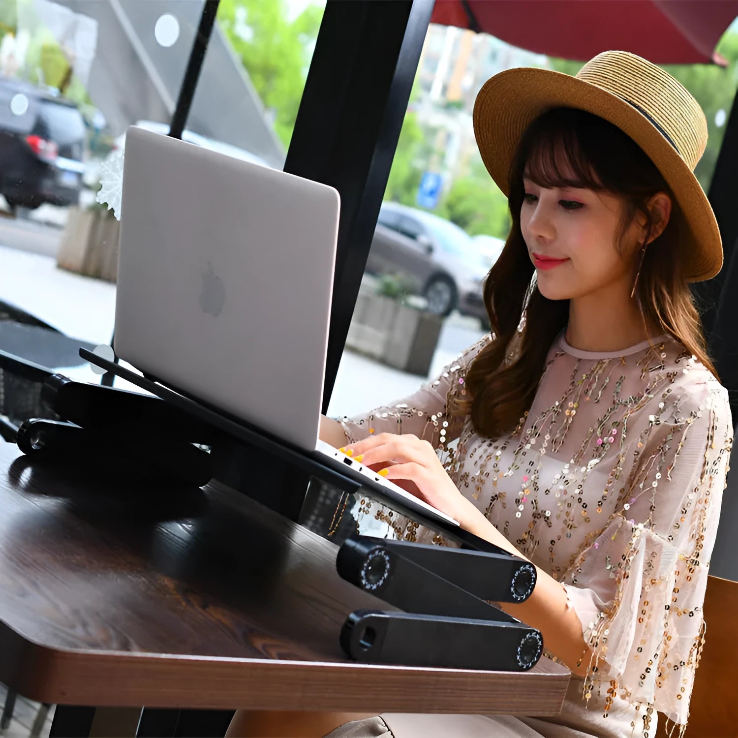 Black folding metal laptop desk with cooling holes extended over a bed.