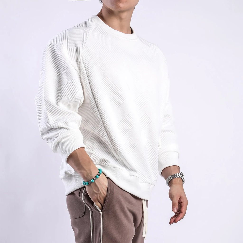 Man wearing a loose grey twill jacquard pullover sweater with a round neck and long sleeves.