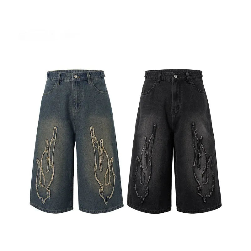 Men's black cropped denim shorts with a flame embroidery patch on the leg, showing straight cut.