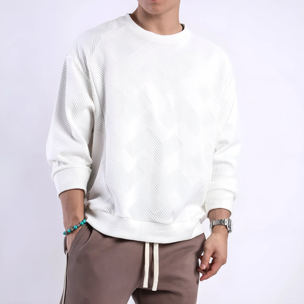 Man wearing a loose grey twill jacquard pullover sweater with a round neck and long sleeves.