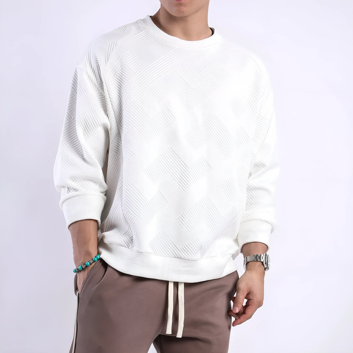 Man wearing a loose grey twill jacquard pullover sweater with a round neck and long sleeves.