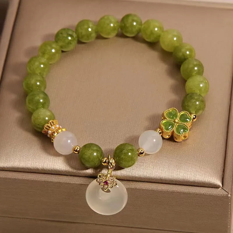 Women's green tourmaline bracelet with a four-leaf clover charm and safety buckle on a wrist.