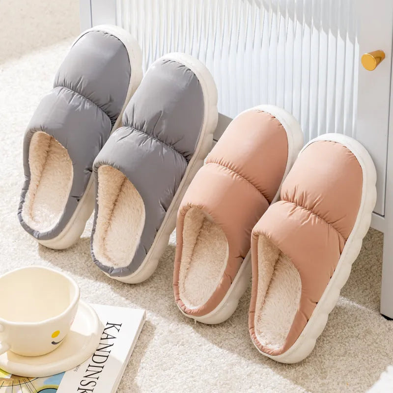 A pair of blue down cotton plush slippers with a thick rubber sole and artificial leather upper, shown on a wooden floor.