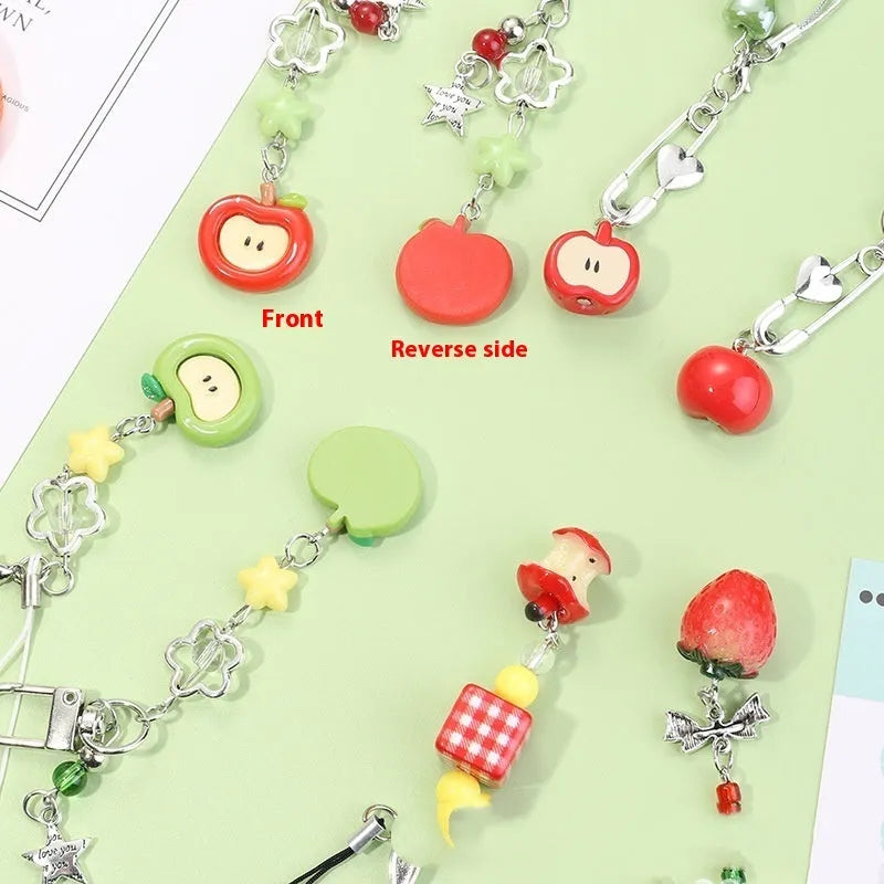 Red apple and strawberry plastic phone charm keychain with white rope on a mobile phone.