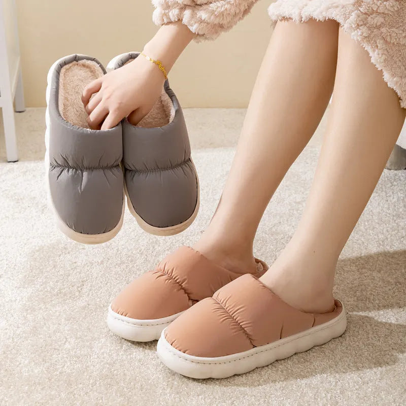 A pair of blue down cotton plush slippers with a thick rubber sole and artificial leather upper, shown on a wooden floor.