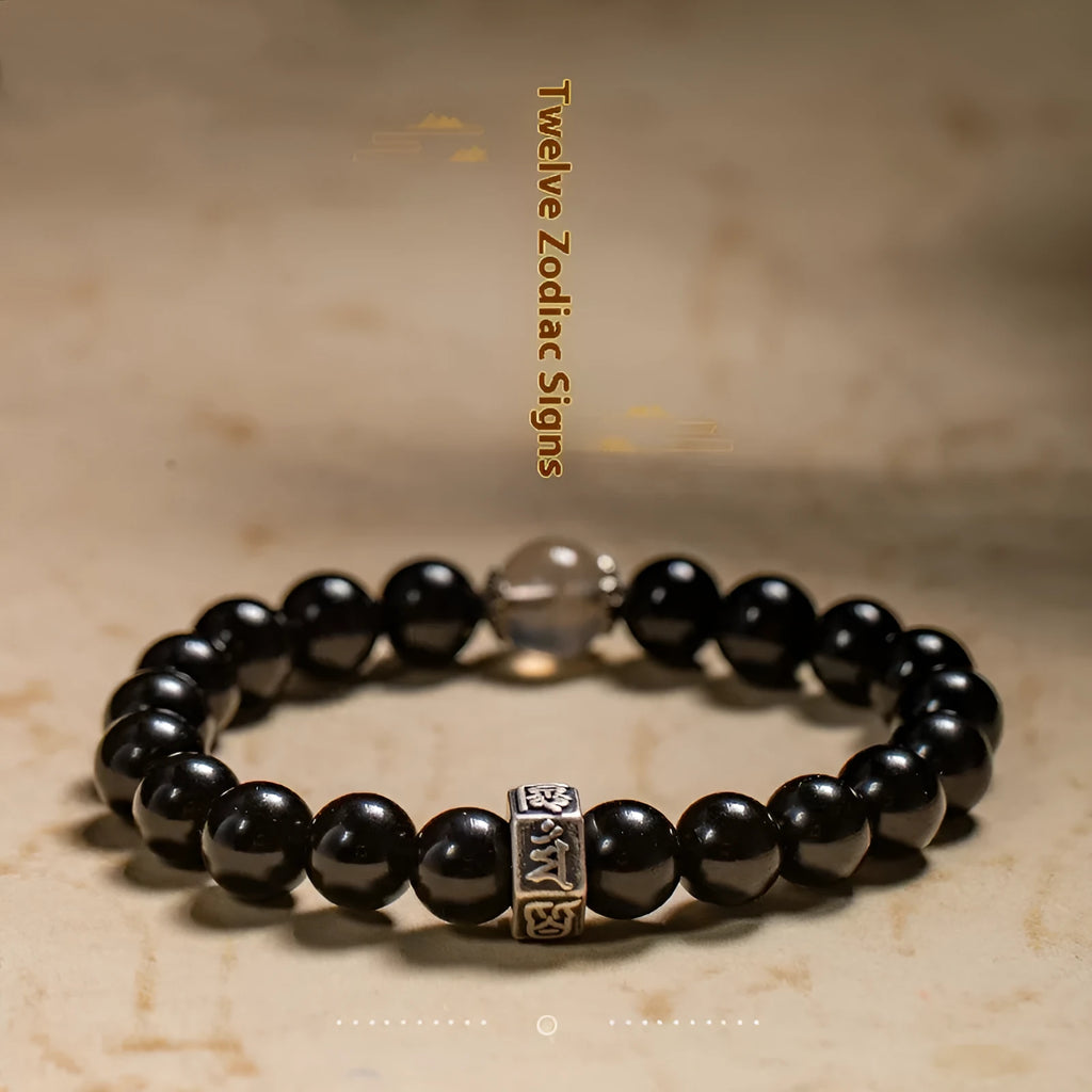 Old Pit Obsidian 8mm bead bracelet with zodiac animal charms on a wrist, showing ethnic style and unset inlaid design.