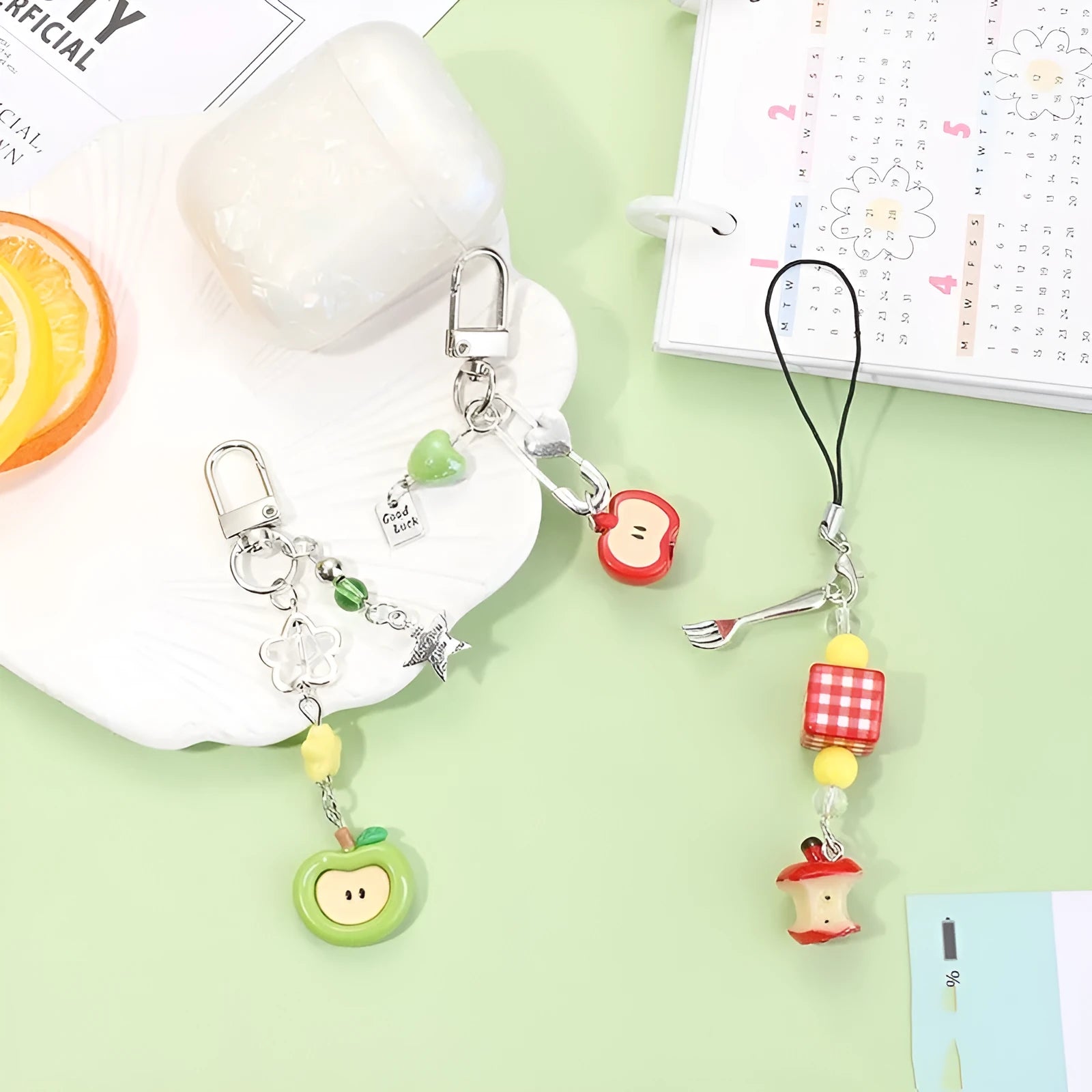 Red apple and strawberry plastic phone charm keychain with white rope on a mobile phone.