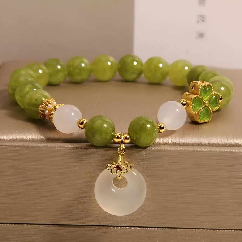 Women's green tourmaline bracelet with a four-leaf clover charm and safety buckle on a wrist.