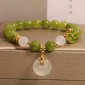 Women's green tourmaline bracelet with a four-leaf clover charm and safety buckle on a wrist.