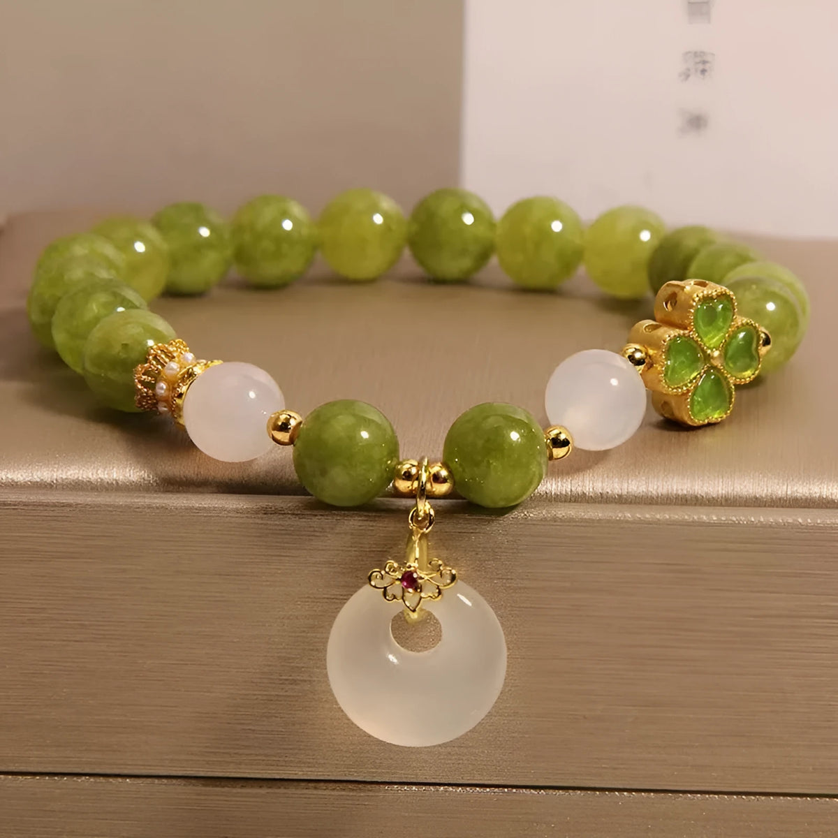 Women's green tourmaline bracelet with a four-leaf clover charm and safety buckle on a wrist.