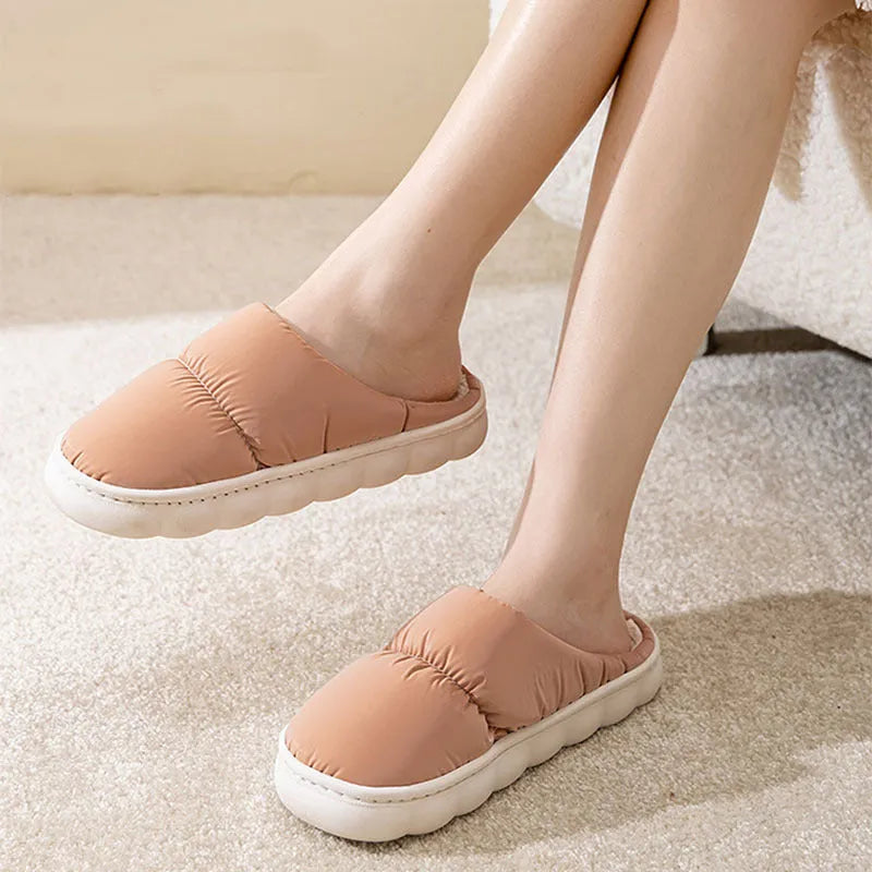 A pair of blue down cotton plush slippers with a thick rubber sole and artificial leather upper, shown on a wooden floor.