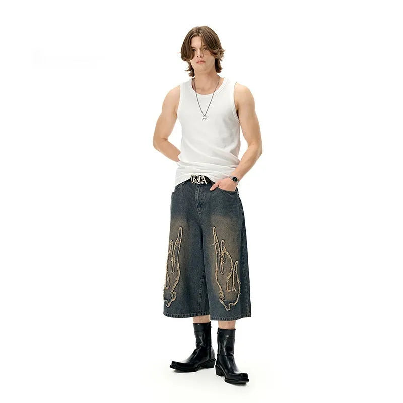 Men's black cropped denim shorts with a flame embroidery patch on the leg, showing straight cut.