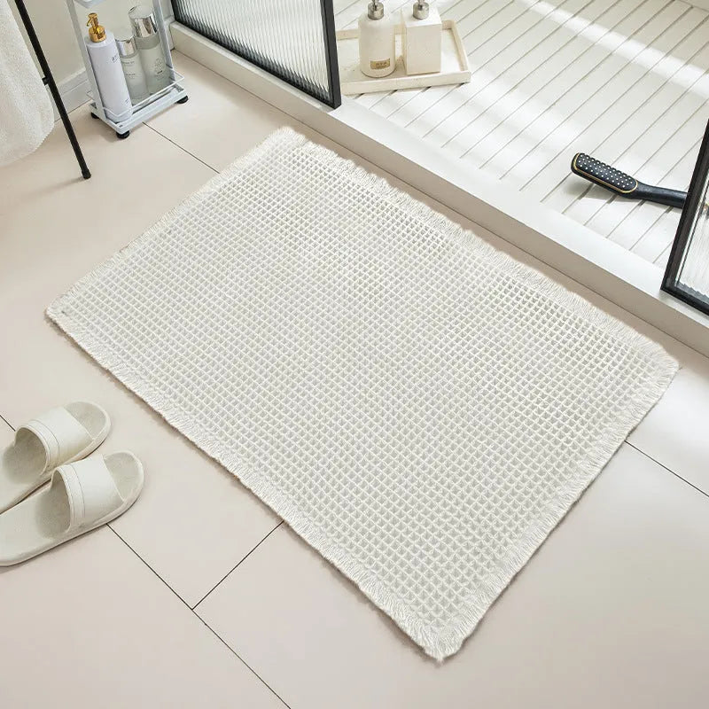 Beige and white checkered woven polyester bathroom floor mat on tiles.